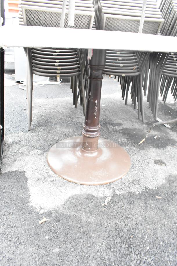 Dining height table with a round metal base, accompanied by stacked chairs, shown on an outdoor surface.