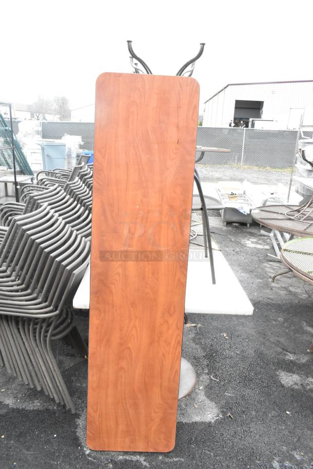 Wooden folding table with metal legs, stacked black metal dining chairs, and thin table seen in outdoor setting.