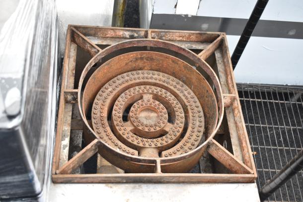 Commercial gas-powered single burner range with a rustic appearance and visible signs of wear. Suitable for heavy-duty use.