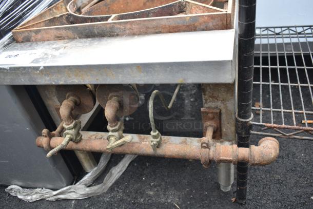 Commercial gas-powered single burner range with rusted components. Metal construction, visible valves and piping. Used condition.