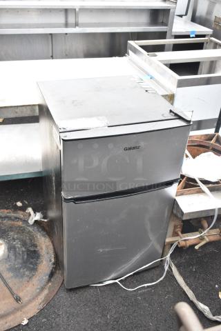 Galanz GLR31TS1E02 mini cooler with freezer, gray finish, visible wear. Model and brand name on front. 115 Volts, 1 Phase.