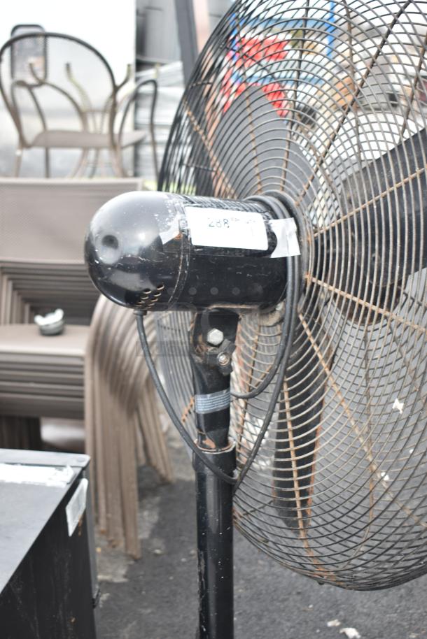 Lasko floor fan with a black metal frame, 115 volts, 1 phase, visible wear on the stand, and a white label on the motor.