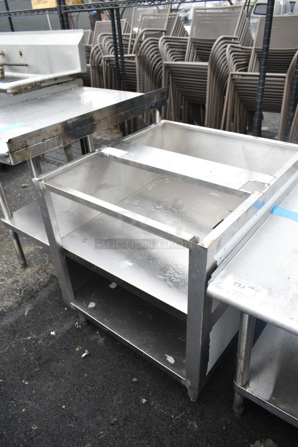 Commercial equipment stand with under shelves, stainless steel, sturdy construction, visible wear, ideal for kitchen use.