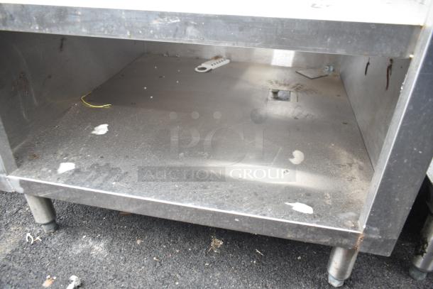 Commercial equipment stand with under shelves, stainless steel, visible wear and tear, sturdy metal construction.