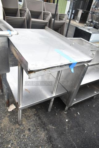 Commercial stainless steel table with under shelf, worn condition, visible dents, and tape on surface.
