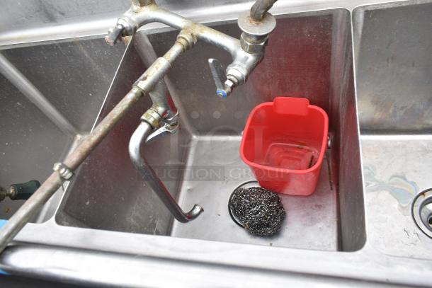 Commercial 3 bay sink with dual faucets, showing used condition. Includes a red container and steel wool pad.