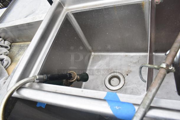 Three-bay stainless steel commercial sink with visible wear, drain, and plumbing fixtures. Used condition.