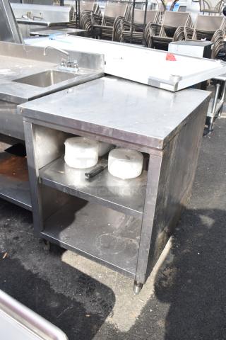Stainless steel commercial table with two under shelves, showing signs of wear, ideal for kitchen use.