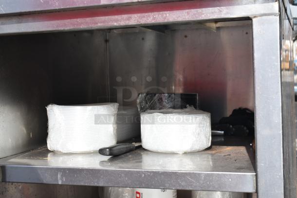Stainless steel commercial table with two under shelves, showing plates and utensils. Good condition, ideal for kitchen use.