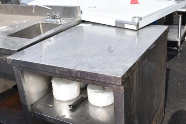 Commercial stainless steel table with under shelves, integrated sink, moderate wear, ideal for industrial kitchens.