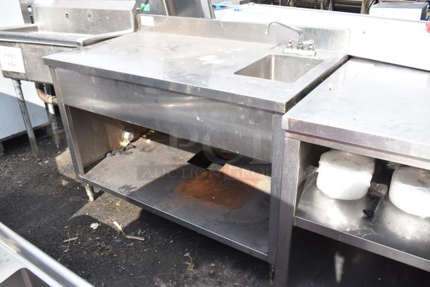 Commercial stainless steel table with sink bay and under shelf, showing signs of use; sturdy design for kitchen settings.