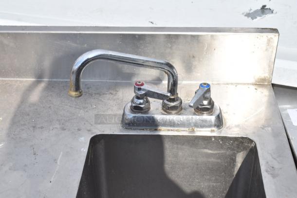 Commercial stainless steel table with integrated sink bay, dual handle faucet, and undershelf. Signs of use visible.