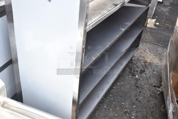 Stainless steel commercial shelving unit, four shelves, industrial-grade. Visible wear and some residue on surfaces.