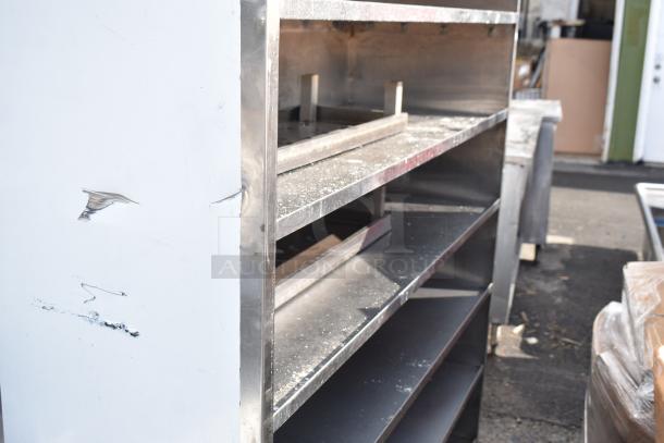 Commercial metal shelving unit, four shelves, visible scuffs and marks indicating wear, durable industrial design.