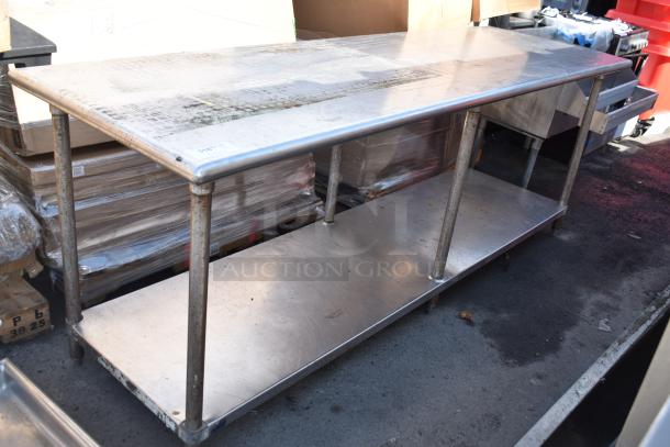 Stainless steel commercial table with lower shelf, visible wear, sturdy design, suitable for kitchen or industrial use.