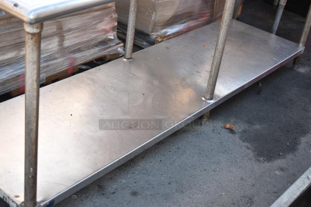 Stainless steel commercial table with under shelf, showing wear. Robust metal legs, ideal for kitchen or café use.