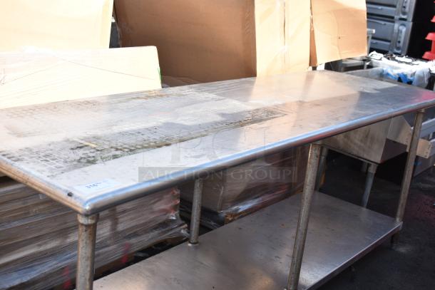 Commercial stainless steel table with under shelf, used condition, visible scuff marks, suitable for kitchen or workshop use.