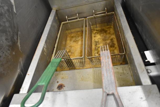Dean Commercial Floor Style Deep Fat Fryer with dual fryer baskets, visible oil and signs of use, metal and green handles.