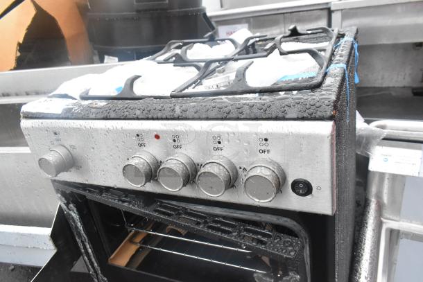4 Burner range with oven, visible water droplets, and oven door damage. Control knobs intact. Auction item.