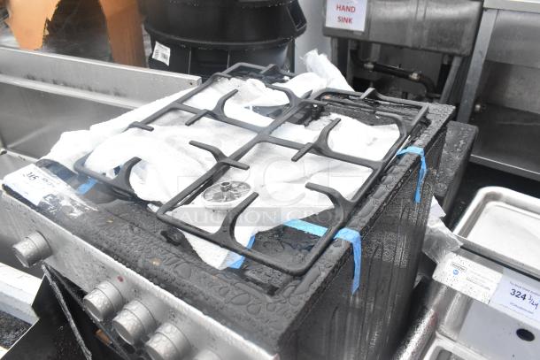 4-burner range with oven, showing top burners. Note visible oven door damage. Visible labels indicate auction details.