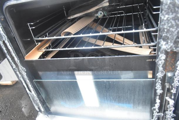 4 Burner Range with Oven showing interior. Note damage on oven door. Features include two racks and cardboard packaging remnants inside.