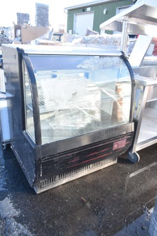 Turbo Air commercial deli display case with curved glass front, black frame, visible wear, and internal shelves.