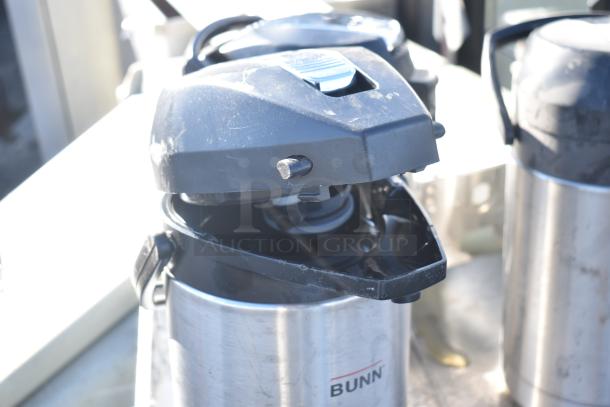 Three stainless steel Bunn countertop air pots with black lids, showing moderate wear, ideal for convenient beverage dispensing.
