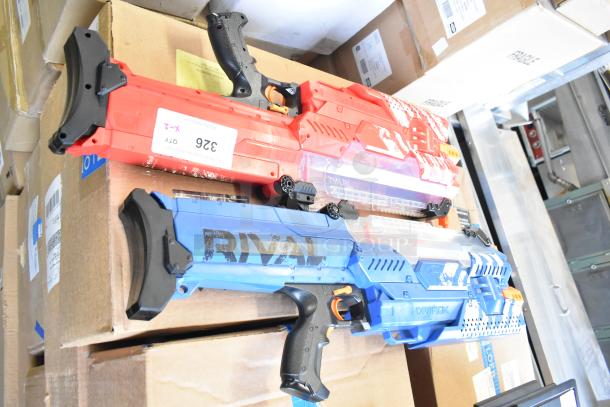 Two Nerf Rival toy guns, one red, one blue, with ergonomic grips. Both appear in good condition, resting on cardboard boxes.
