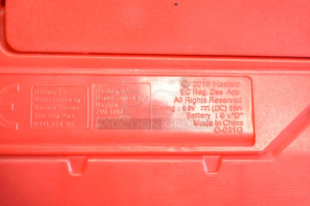 Close-up of red plastic showing Hasbro labeling. Details include manufacturer information, copyright, and battery specifications.