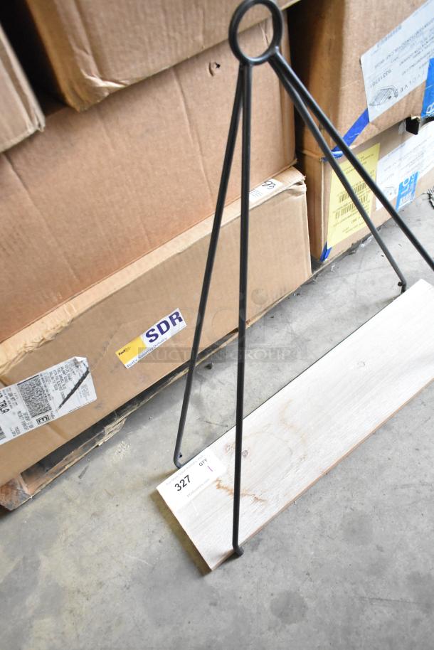 Metal stand with triangular frame and wooden base, item tag 327, placed against cardboard boxes; sturdy and industrial design.