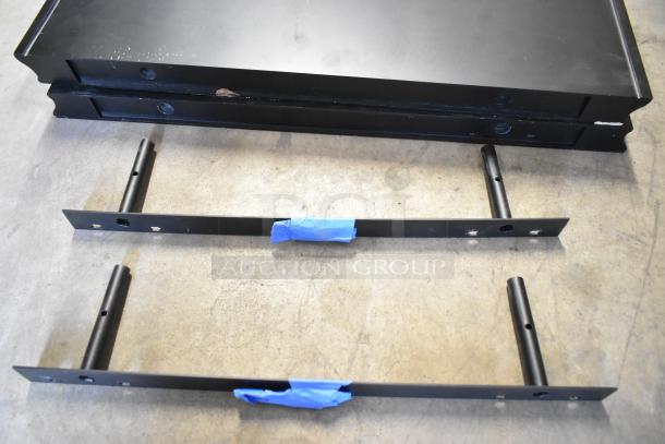 Two black metal shelves with brackets, minor wear, taped sections. Auction includes two units, bid multiplier applies.