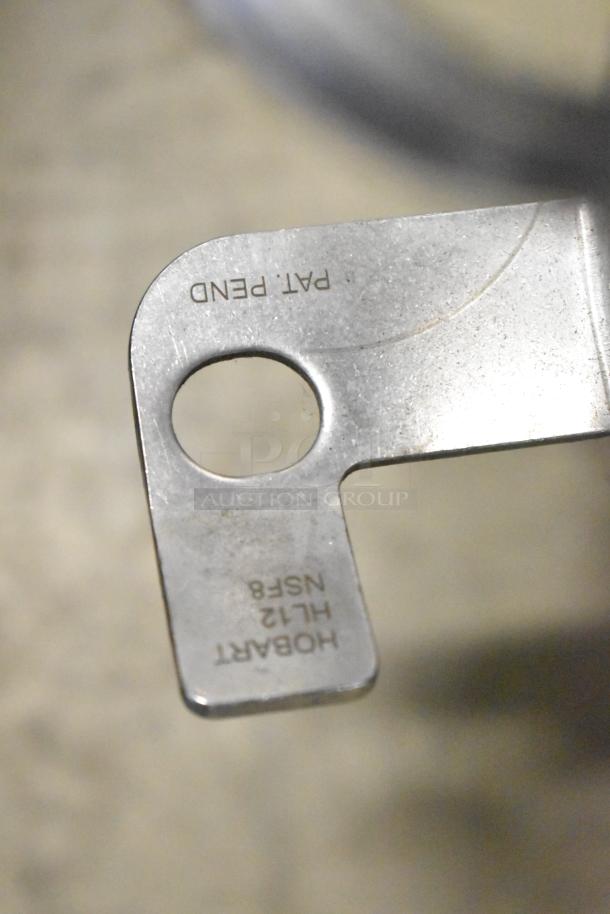 Metal component of Hobart HL12 mixer accessory showing "HOBART HL12 NSF8" and "PAT PEND" markings, indicating model and status.