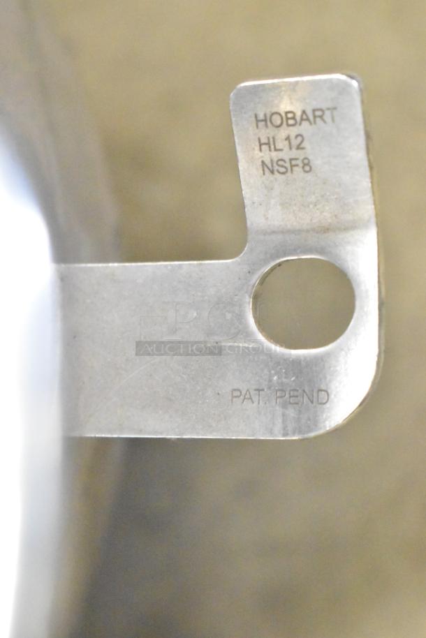 Close-up of Hobart HL12 mixer accessory showing marking "HOBART HL12 NSF8 PAT PEND" indicating compatibility and certification.