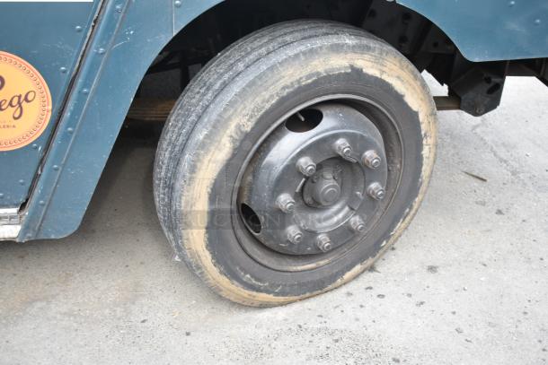 Freightliner food truck tire, slightly worn, on a blue panel. Visible logo sticker and metal bolts.