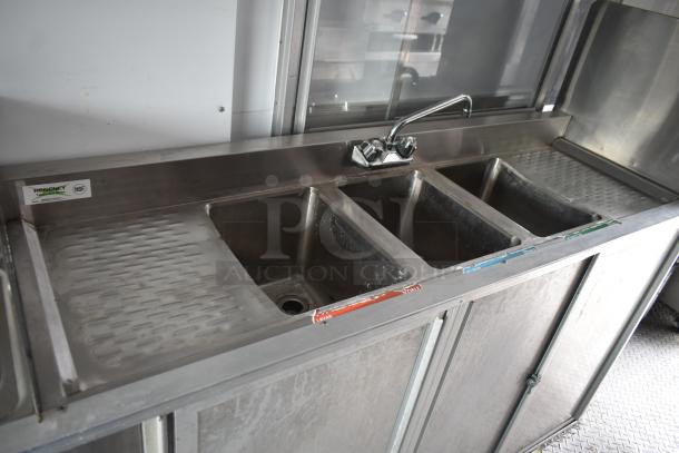 Stainless steel triple sink with workspace in a 2002 Freightliner food truck. Features labeled hot, cold, and soapy water. NSF certified.