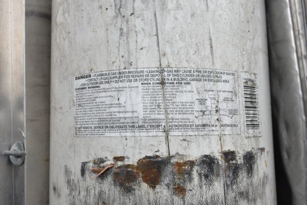 Rusty propane tank with safety label attached, emphasizing flammable gas warning and proper use instructions.