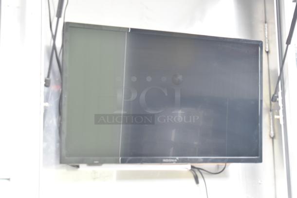 A blurry image of a wall-mounted Insignia screen with visible cables against a metallic background.