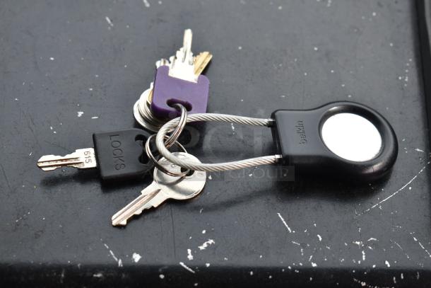 Keys on a ring with a purple tag and a Belkin keychain cable lock, placed on a black surface.