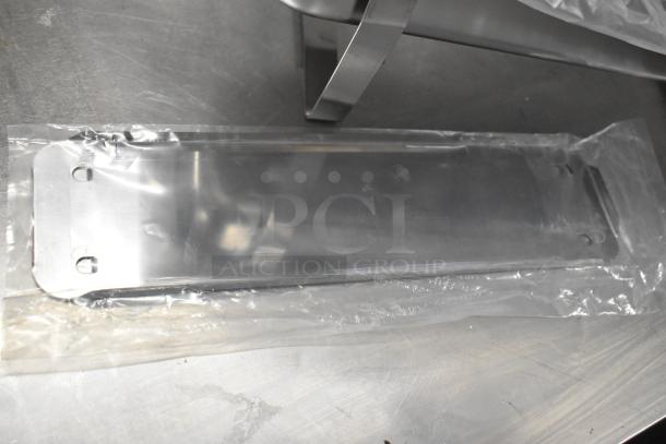 18 brand new scratch and dent items including chafing dish frames and lids in plastic wrap on a metal surface.