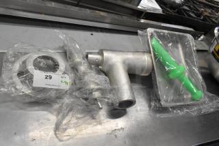 Brand new scratch and dent meat grinder attachment with auger, tray, and green pusher, wrapped in plastic. Lot tag 29 visible.