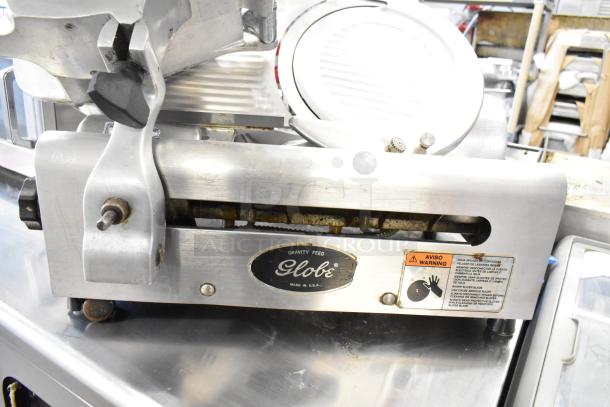 Globe commercial meat slicer with blade sharpener, 115 volts, 1 phase. Features safety labels and "Made in U.S.A." marking.