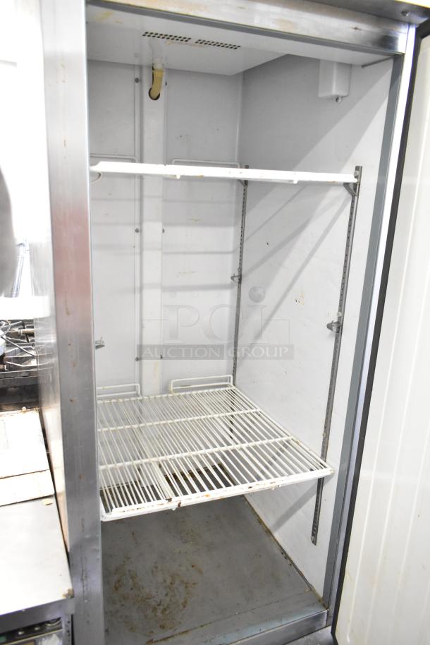 Arctic Air AR23E commercial cooler, single door, interior shelving, visible wear, model label indicating 115 volts, 1 phase.