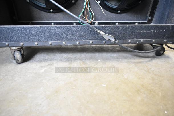 Roland Jazz Chorus 120 speaker on casters, showing wheel and cable, black textured exterior, moderate wear.