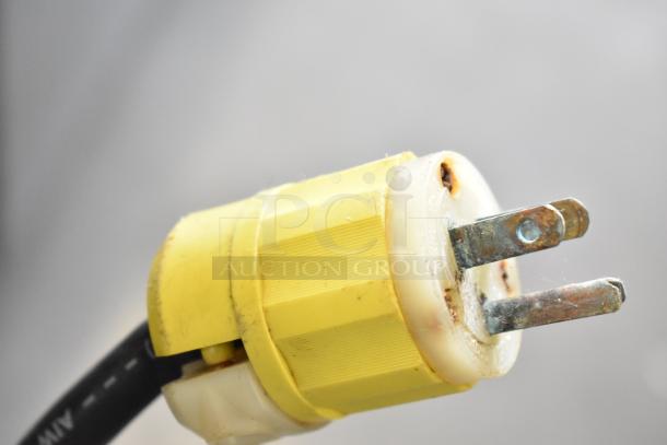 A close-up of a worn yellow electrical plug with visible rust on the metal prongs.