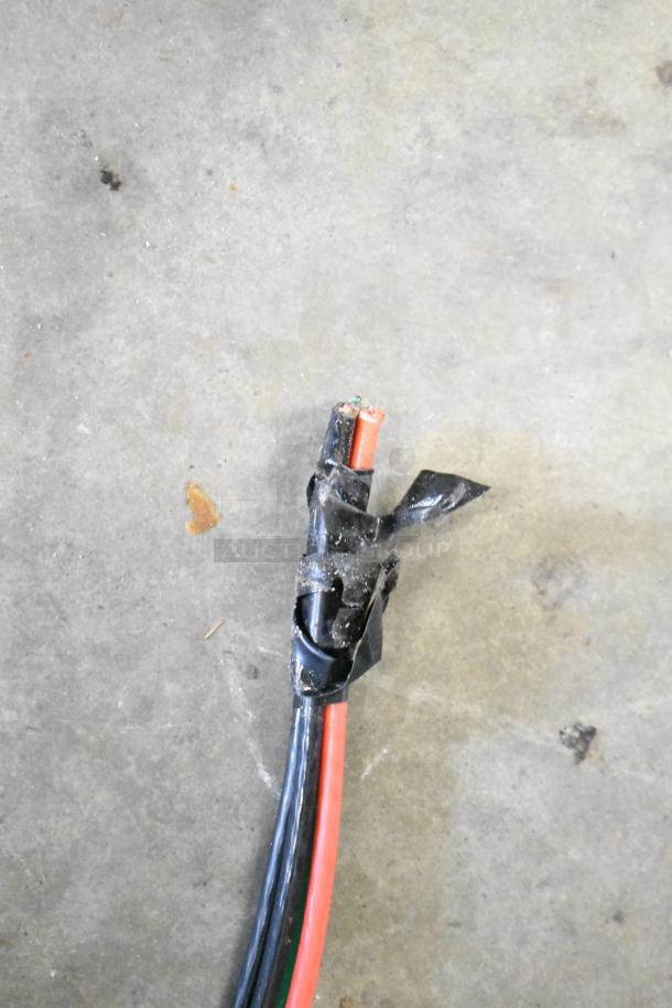 Frayed electrical cord with exposed wires and black tape on concrete surface.