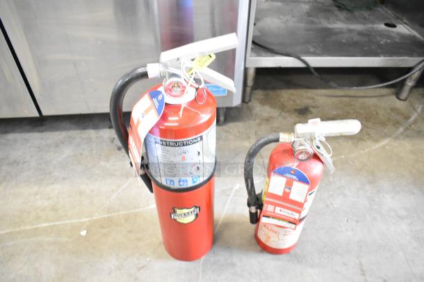 Two fire extinguishers, including a Buckeye model, red with instruction labels. Buyer pick-up only; not for shipping.