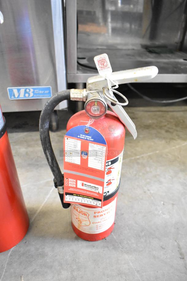 Red Buckeye fire extinguisher with pressure gauge, safety tags, and label markings indicating multi-use. Buyer pick-up required.