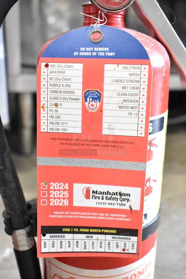 Red fire extinguisher from Buckeye, labeled by FDNY. Tag shows service compliance marks by Manhattan Fire & Safety Corp.