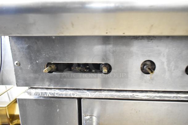 American Range commercial gas 6-burner stove with oven, featuring overshelf and backsplash. Metal surface, well-used condition.