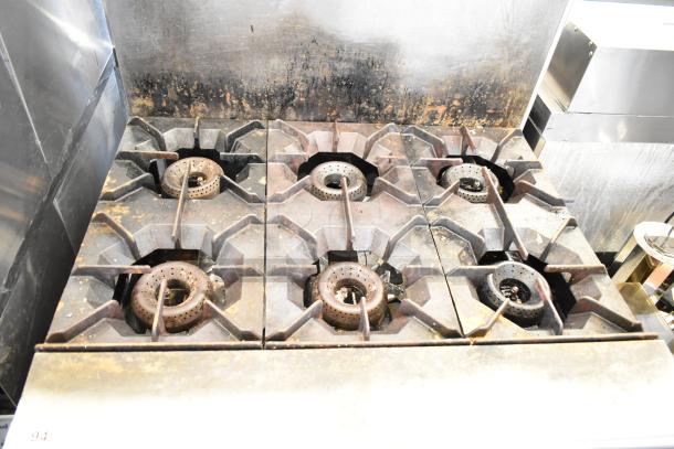 American Range commercial gas-powered 6-burner range with oven and backsplash. Visible wear consistent with use.